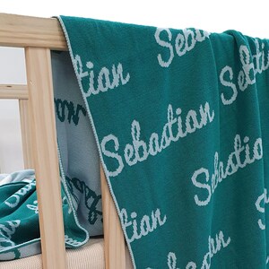 May include: A teal blue knitted baby blanket with the name "Sebastian" embroidered in white on it.