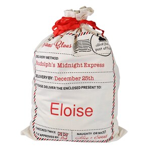 May include: A white canvas Santa sack with red trim and a red ribbon. The sack has a label that says "Santa Claus" and "Rudolph's Midnight Express". The label also says "Delivery by: December 25th" and "Please deliver the enclosed present to: Eloise".