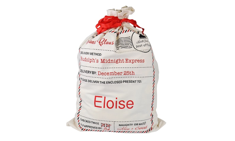 May include: A white canvas Santa sack with red trim and a red ribbon. The sack has a label that says "Santa Claus" and "Rudolph's Midnight Express". The label also says "Delivery by: December 25th" and "Please deliver the enclosed present to: Eloise".