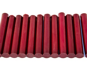 May include: A collection of eleven cylindrical, burgundy-colored wax sticks arranged horizontally against a white background. The wax sticks have a smooth, glossy finish and are evenly spaced.