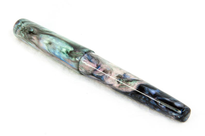 K&ouml;nnte beinhalten: Eine wei&szlig;e Keramik-Tasse mit schwarzem Henkel und dem Text "But First, Coffee" in fetter, schwarzer Schrift. Die Tasse steht vor einem verschwommenen Hintergrund, der eine gem&uuml;tliche Umgebung andeutet.