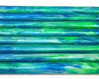 May include: A collection of cylindrical wooden dowels with a marbled effect. The dowels are painted in shades of blue and green, creating a swirling pattern. The dowels are arranged horizontally, showcasing their colorful design.