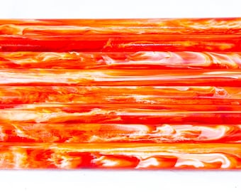 May include: A collection of orange and white swirled resin rods. The rods are cylindrical and appear to be stacked, showcasing a vibrant, marbled effect. The color palette includes shades of orange, red, and white.