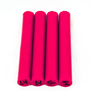 May include: Four bright pink cylindrical objects are arranged vertically against a white background. Each cylinder has a rounded top and a flat bottom with black markings. The objects appear to be made of a solid material.