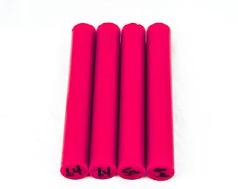 May include: Four bright pink cylindrical objects are arranged vertically against a white background. Each cylinder has a rounded top and a flat bottom with black markings. The objects appear to be made of a solid material.
