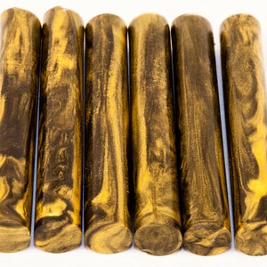 May include: Six golden brown and black marbled acrylic pen blanks. The blanks have a swirling pattern of gold and black.