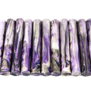 May include: A collection of cylindrical wax sticks with a marbled design. The sticks feature a blend of purple, black, and white hues. The wax sticks are arranged horizontally against a white background.