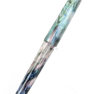 K&ouml;nnte beinhalten: Ein marmorierter F&uuml;llfederhalter mit Kappe. Der Stiftk&ouml;rper weist eine Mischung aus Farben auf, darunter Blau, Gr&uuml;n und Rosa, wodurch ein einzigartiges, wirbelndes Muster entsteht. Der Stift ist vor einem wei&szlig;en Hintergrund platziert.