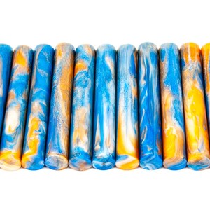 May include: A collection of twelve cylindrical objects with a marbled design. The colors are blue, orange, and white, creating a swirling pattern. The objects are arranged horizontally against a white background.