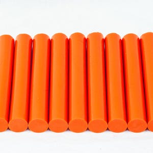 May include: A collection of eleven bright orange cylindrical objects, arranged in parallel rows. Each cylinder has a rounded top and bottom, and the objects are evenly spaced against a white background. The objects appear to be made of a solid material.