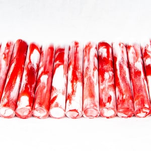 May include: A collection of cylindrical, red and white swirled objects. The objects are arranged in a row against a white background. The red and white colors are mixed, creating a marbled effect.