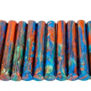 May include: A row of 12 colorful resin pen blanks with a copper, blue, and green marbled pattern.