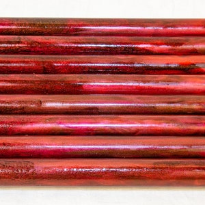 May include: A stack of ten red and brown wooden dowels. The dowels have a marbled appearance and are arranged in a neat row.