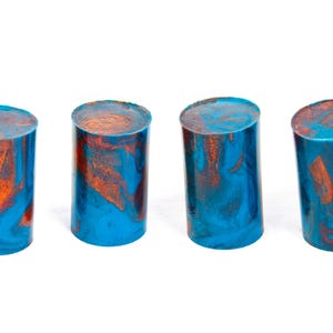 Puede incluir: Cuatro objetos cilíndricos con un diseño veteado. Los cilindros son principalmente azules con remolinos naranjas y cobrizos. Los objetos están de pie sobre un fondo blanco.