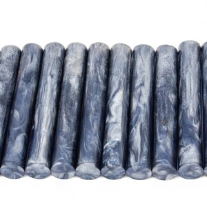 May include: A row of 15 blue and white marbled acrylic pen blanks. The blanks are cylindrical and have a swirling pattern of blue and white.