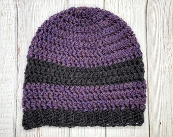 May include: A handmade crochet beanie in shades of purple and black. The hat features a ribbed brim and a textured stitch pattern. The color gradient transitions from purple to black, creating a visually appealing design. This warm hat is perfect for cold weather.