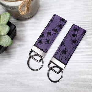 May include: Two purple keychains with black spider patterns and silver key rings.