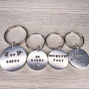 May include: Four silver keychains with different phrases engraved on them. The phrases are "Oh Daddy", "Oh Daddy", "Absolute Twat", and "Jizzys Revenge".
