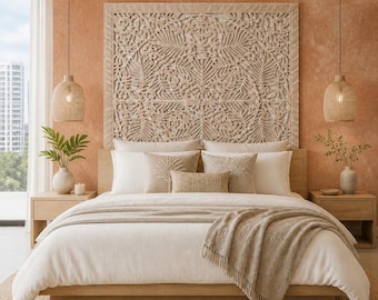 May include: A large, rectangular, light-colored wooden headboard featuring intricate, symmetrical floral and leaf carvings. The bed is dressed in white linens, a beige throw blanket, and several decorative pillows in shades of cream and tan.