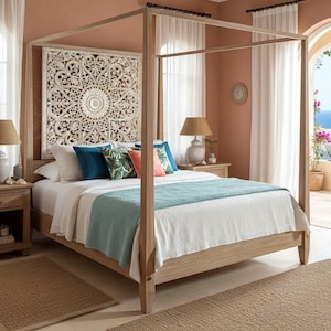May include: A light wood canopy bed frame with a tall, square post design. Behind the bed, a large, square, white-washed wooden wall panel features an intricate, symmetrical, carved floral mandala pattern with a central circular motif.