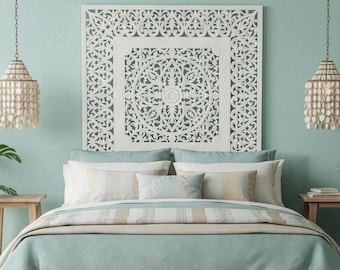 May include: A bedroom set featuring a light-colored wooden bed frame with a light blue duvet and pillows. Above the bed is a large, square, white carved wooden wall panel with intricate floral patterns. Two hanging pendant lights with shell accents.