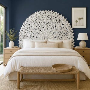 May include: A large, semi-circular white carved wooden headboard featuring intricate floral and scrollwork patterns. The headboard is positioned behind a bed with white bedding, beige accent pillows, and a woven bench at the foot of the bed.