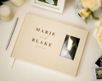 Puede incluir: Un libro de visitas de boda beige con una ventana para una foto. El libro tiene los nombres "Marie y Blake" y la fecha "09.23.24" impresos en la portada.
