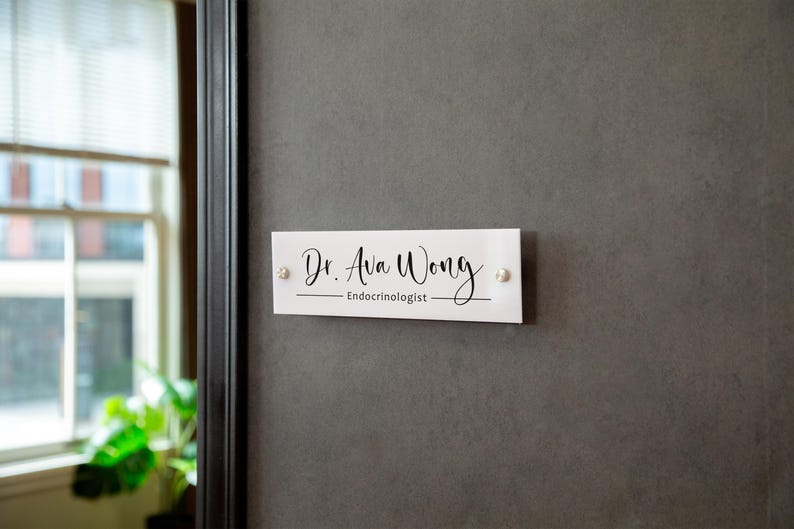 May include: White rectangular sign with black text that reads "Dr. Ava Wong - Endocrinologist".