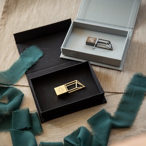 May include: Gold-coloured USB flash drives with geometric designs, presented in black and grey boxes. The boxes are displayed with teal ribbon. The USB drives are ideal for storing data.