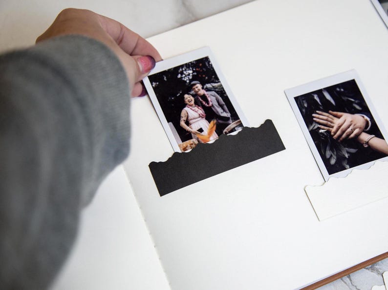 Puede incluir: Un &aacute;lbum de fotos blanco con dos fotos en blanco y negro insertadas. Las fotos son de una pareja y una mano sosteniendo un anillo.