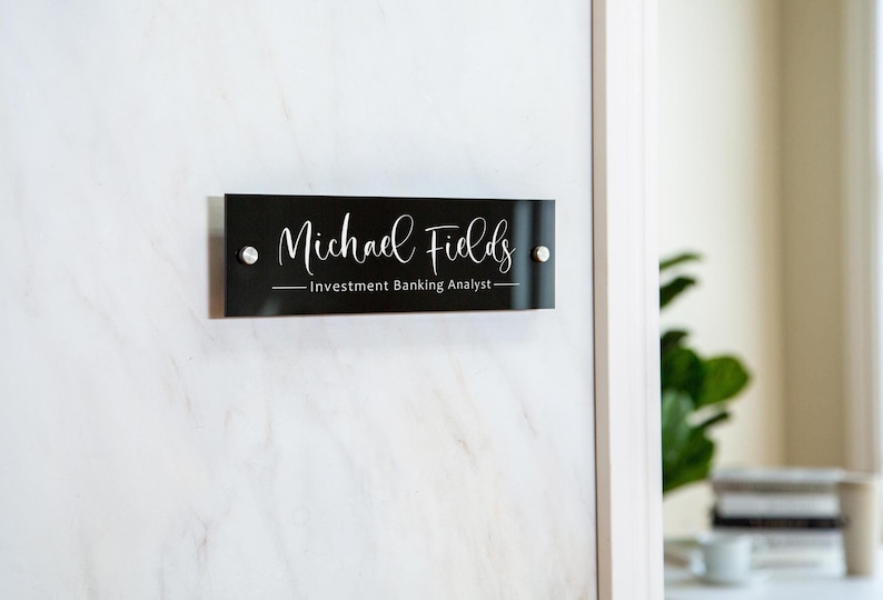 May include: Black rectangular office door sign with silver mounting screws. The sign reads "Michael Fields - Investment Banking Analyst".
