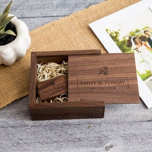 May include: A wooden box with a hinged lid, engraved with the text "Emily & Tommy 09.23.2018" and a floral design. The box contains a wooden USB drive with the same text and design.