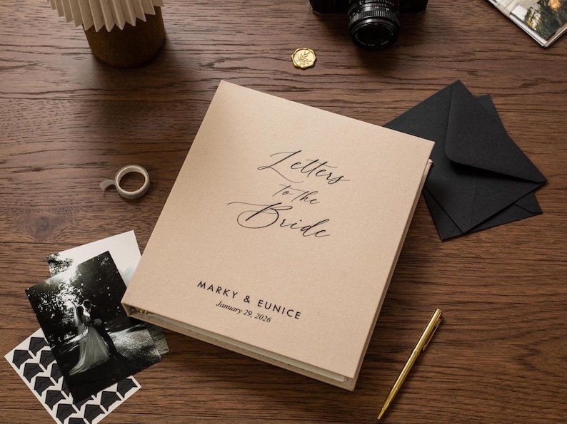May include: A beige wedding keepsake book titled "Letters to the Bride" with the names Marky & Eunice and the date January 29, 2026. The book is on a wooden surface with a pen, photos, and black envelopes.