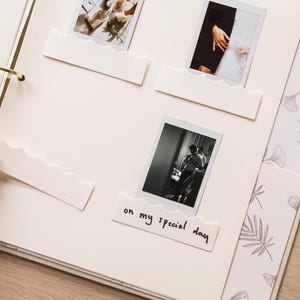 May include: An open scrapbook with gold ring binders, featuring several black and white photographs. White, wave-shaped photo holders are placed around the photos. One holder has the text "on my special day".