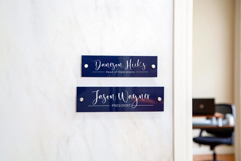 May include: Two blue office door signs with white lettering. The top sign reads "Daneson Hicks - Head of Operations". The bottom sign reads "Jason Wayner - President".