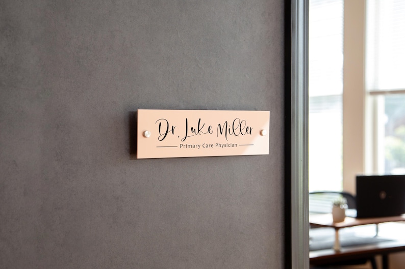 May include: A peach-colored rectangular sign with rounded corners and black text that reads "Dr. Luke Miller - Primary Care Physician".