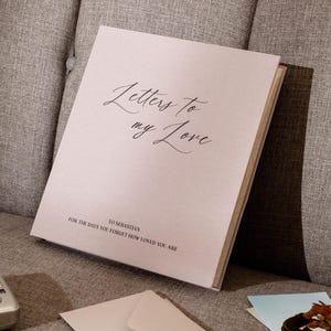 May include: A light beige hardcover book with the text "Letters to my Love" in a black script font on the front cover. Below this, the text reads "TO SEBASTIAN" and "FOR THE DAYS YOU FORGET HOW LOVED YOU ARE" in a simple, clean black typeface.