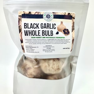 May include: A white, resealable bag of Bisbee Delicatessen Black Garlic Whole Bulb. The label features text and illustrations of garlic bulbs. The bag contains whole, fermented black garlic bulbs. Net weight is 5oz.