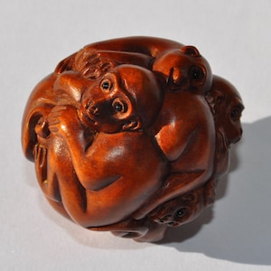 May include: A wooden sculpture of multiple monkeys intertwined in a ball shape. The monkeys are carved from a reddish-brown wood, with visible details of their faces and bodies. The sculpture is a detailed, handcrafted piece.