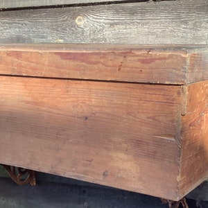 May include: A vintage wooden box with a hinged lid and metal brackets. The box is made of natural wood with a rustic finish.