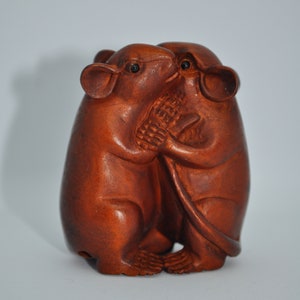 Puede incluir: Escultura de madera de color marrón rojizo que representa dos ratones abrazados. Los ratones están tallados con detalle, mostrando sus patas, orejas y caras juntas. La escultura es de madera y tiene un acabado liso.