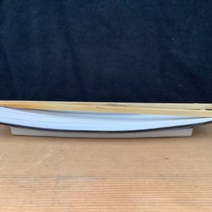 May include: A white rectangular sushi plate with a black trim, holding two wooden chopsticks. The plate has a slightly curved design. The chopsticks are light brown and rest parallel to each other on the plate.