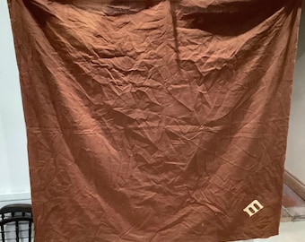 May include: A large, brown fabric backdrop with a single, white letter "M" in the lower right corner.