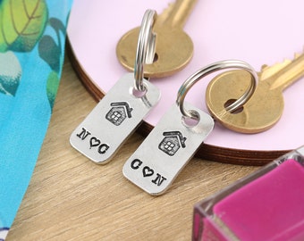 May include: Two silver keychains with house and heart designs. The keychains are engraved with the initials "N" and "C" and the text "N ♥ C" and "C ♥ N".