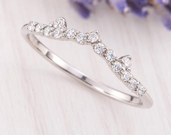 Può includere: Un anello color argento caratterizzato da una fascia curva e dentellata, incastonata con una serie di piccole pietre chiare a taglio rotondo. Il design segue un contorno delicato e asimmetrico con diverse pietre lungo il bordo superiore.