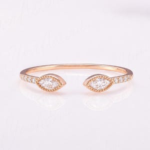 May include: An open-style rose gold ring featuring two marquise-cut clear stones at the ends, each surrounded by a beaded metal border. The band is accented with small, round, clear pavé-set stones along the sides of the ring shank.