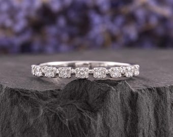 May include: A silver-toned band ring featuring a series of small, round, clear stones set in individual square-shaped metal frames that span across the top half of the band, creating a continuous, sparkling, and detailed design.