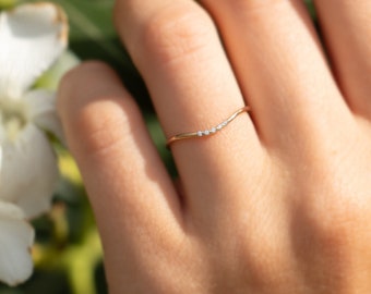 May include: A delicate gold band ring with a curved line of small diamonds.