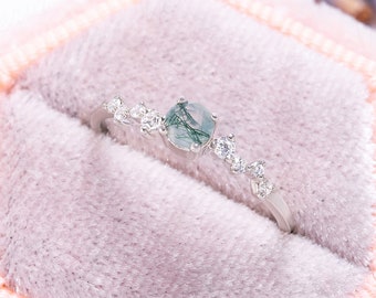 May include: A silver ring with a green moss agate gemstone and small clear stones set in a pink velvet ring box.