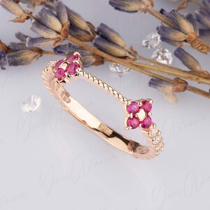 May include: A rose gold ring with a floral design. The ring features a cluster of pink gemstones in a four-petal flower shape, with a band adorned with small white gemstones. Dried lavender sprigs and small crystals are in the background.